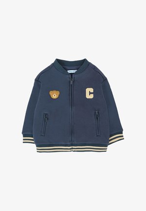 Giubbotto blu navy con zip realizzato in morbido tessuto. Presenta una toppa d'oro a forma di orso, una lettera "C" e polsini e orlo a righe. Due tasche con zip.