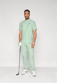 Ανοιχτό πράσινο σύνολο για γκολφ με κοντομάνικο πουκάμισο με υφή και παντελόνι που ταιριάζει, συνδυασμένο με λευκά αθλητικά παπούτσια και μπαστούνι γκολφ.