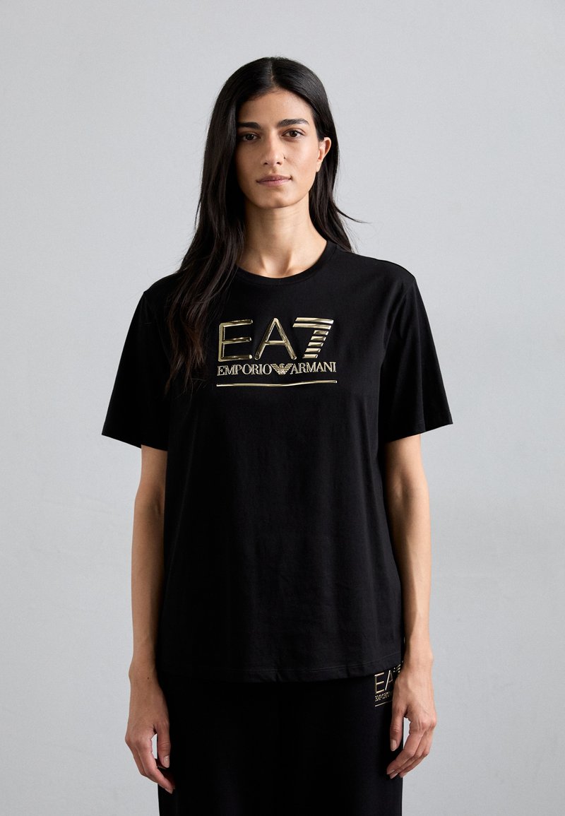 Crna pamučna majica s okruglim izrezom i kratkim rukavima. Sadrži zlatni EA7 Emporio Armani logo otisnut na prednjoj strani.