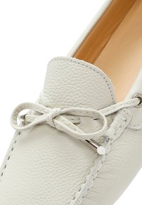 Zapato náutico blanco de cuero con acabado texturizado, presenta un detalle de lazo a juego y herrajes en tono plateado, con acentos cosidos a lo largo de los bordes.