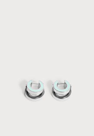 Silberne Creolen mit einem hellblauen Email-Halbmond-Design oben vor einem schlichten hellen Hintergrund.