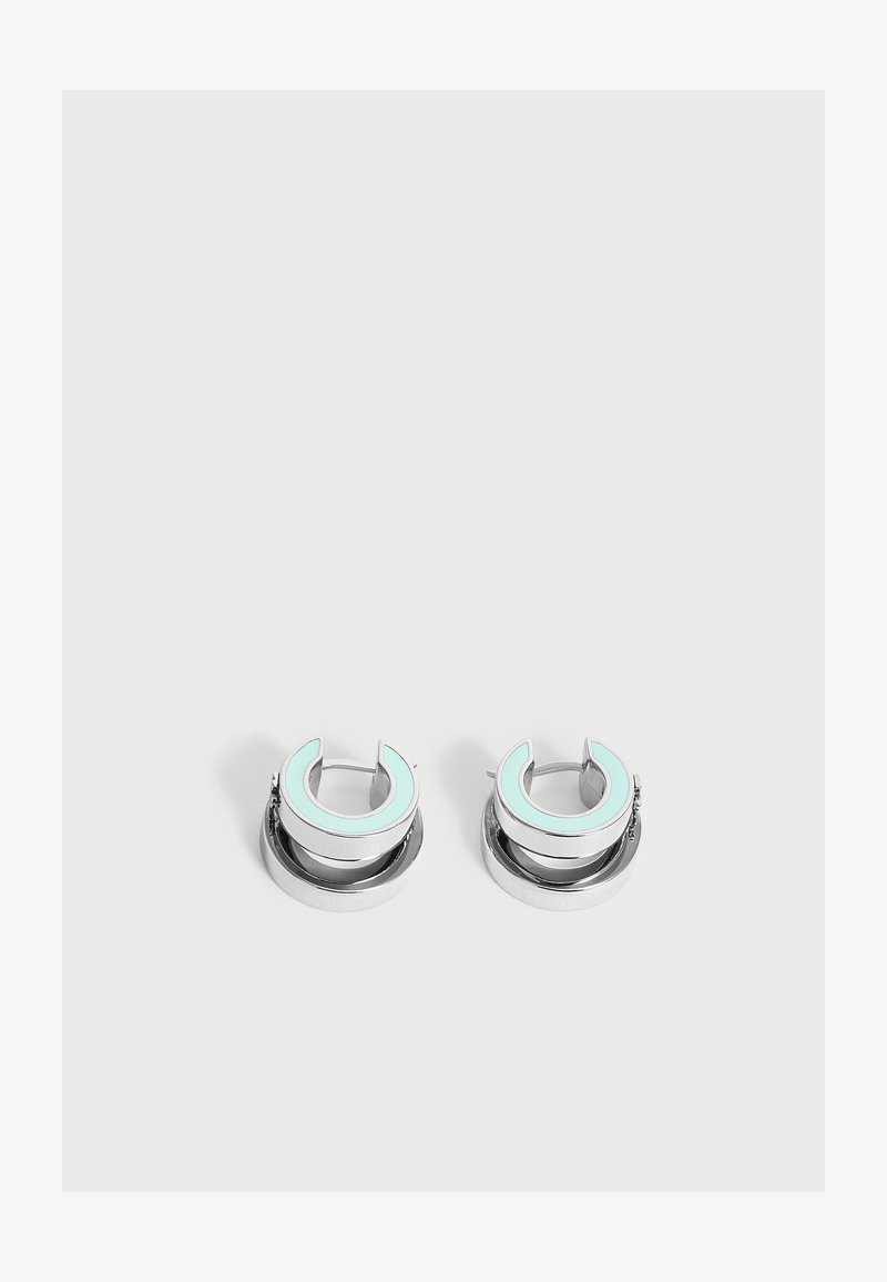Boucles d'oreilles créoles en argent avec un motif croissant de lune en émail bleu clair sur un fond clair uni.