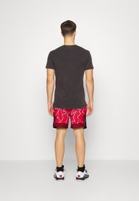 Mörkgrå t-shirt med kort ärm i kombination med röda mönstrade shorts som har zick-zack-mönster och svarta accenter. Vita sneakers fulländar outfiten.