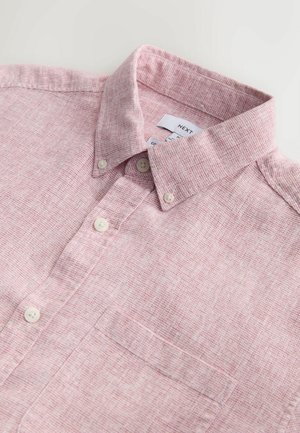 Svetlo roza srajca s teksturirano tkanino, kratkim ovratnikom in levim prsni žep. Ima bele gumbe in subtilen vzorec.
