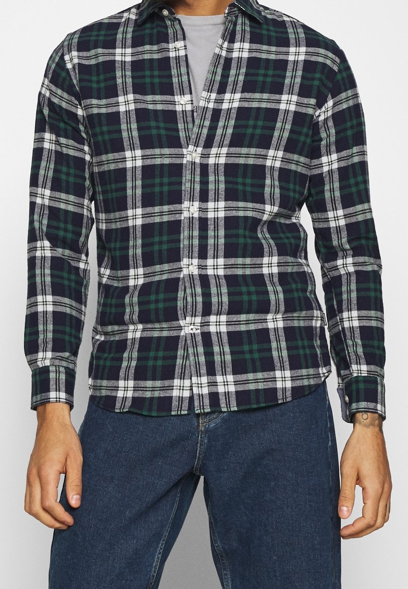 Miesten ruudullinen paita, jossa on vihreitä, laivastonsinisiä ja valkoisia värejä, napitus, pitkät hihat ja rento fit sekä kaareva helma.