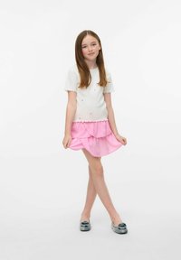 Top blanco de manga corta con ribetes ondulados, combinado con una falda rosa de volantes en capas. Presenta zapatos grises con acentos decorativos.