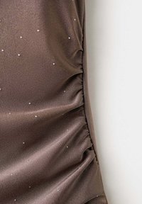 Tissu satin marron avec de petits points argentés dispersés et des coutures froncées le long d’un bord, sur fond blanc.
