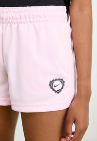 Světle růžové sportovní šortky s elastickým pasem, s černým logem Nike uvnitř vykrojeného diamantového tvaru. Hladká textilie.