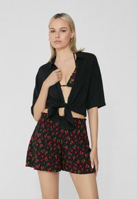 Černý zkrácený top s uzlem na přední straně, v kombinaci s černými šortkami s červeným třešňovým vzorem. Hladká tkanina s uvolněným střihem.