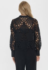 Black lace blouse featuring a high collar, long sleeves, and intricate cut-out patterns resembling peacock feathers. Back is partially sheer.
