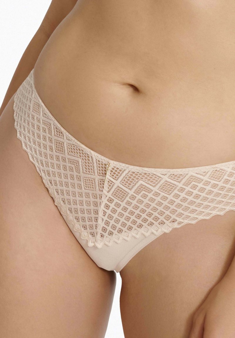 Nudefarbene Spitzenstringtanga mit geometrischen Diamantmustern, gewellten Rändern und einer glatten, matten Textur am Bund.