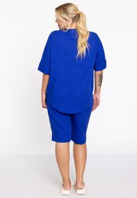 Koninglijk blauwe top met korte mouwen en een ronde zoom, gecombineerd met bijpassende knielange shorts. Het materiaal lijkt textuur te hebben en is lichtgewicht.