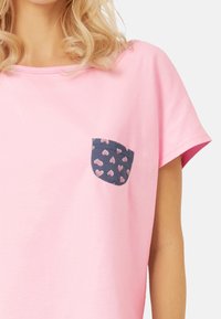 Różowa koszulka z okrągłym dekoltem i krótkimi rękawami, z granatową kieszonką w małe różowe serca. Miękka bawełniana faktura tkaniny.