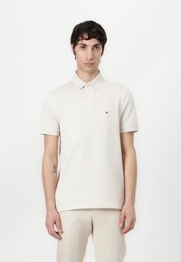 Polo shirt van lichtbeige katoen, met een kraag, korte mouwen en een klein logo op de linkerborst. Glad textuur, getailleerd ontwerp.