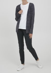 Meriino sininen neulecardigan avonaisella etuosalla, pitkät hihat ja ribattyt hihansuut, yhdistetty valkoiseen t-paitaan ja mustiin housuihin, viimeistelty valkoisilla lenkkareilla.