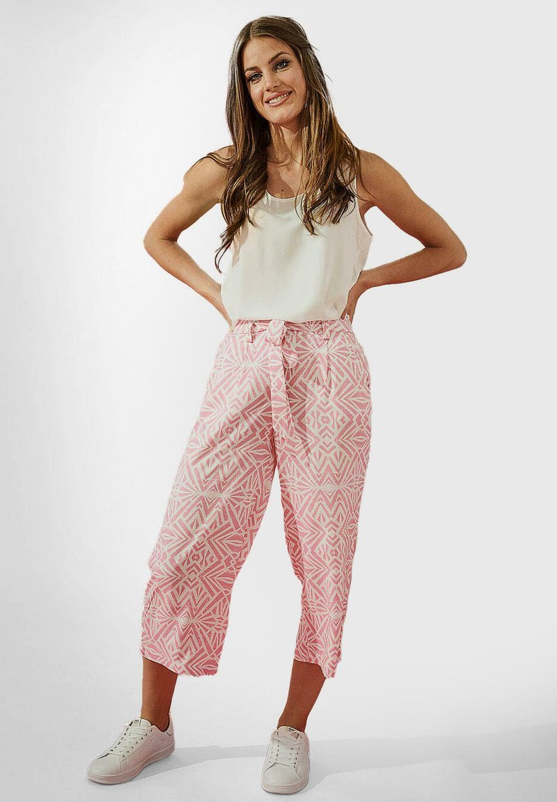 Pantalons courts à motifs roses avec une taille à nœud, associés à un débardeur blanc et des baskets blanches, présentant une coupe décontractée et des motifs géométriques.