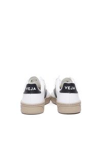 White sneakers with a black heel tab, featuring a logo. Textured white upper and beige rubber sole. Side stripes add detail.