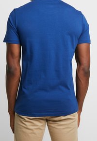 Camiseta de algodón azul con cuello redondo, mangas cortas y un corte ajustado. La tela parece suave con mínimas texturas.