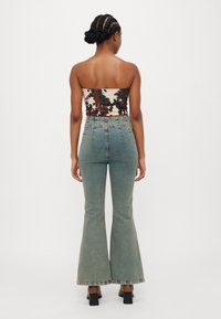Blugi evazați cu talie înaltă, din denim albastru deschis cu o decolorare subtilă. Asociați cu un top fixat, fără bretele, cu un model ce include desene maro și negre.