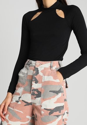 Haut noir à manches longues avec découpes aux épaules, associé à un pantalon camouflage rose taille haute, doté de poches et d'une fermeture à boutons.
