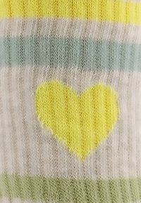 Gestrickte Socken mit einem gestreiften Muster in Gelb, Hellblau und Beige, mit einem zentralen gelben Herzdetail. Weicher Stoff und gerippte Gestaltung.
