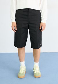 Black knee-length shorts, flat front with two side pockets, made of sturdy fabric. Paired with light green sneakers and white socks.