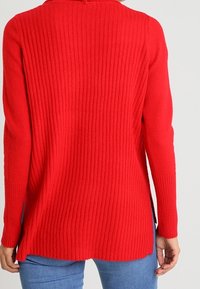 Punainen ribbitekniikalla neulottu villapaita, jossa on pitkät hihat, sivuaukot ja pyöreä pääntie. Pehmeä rakenne ja rento leikkaus lisäävät mukavuutta ja liikkuvuutta.