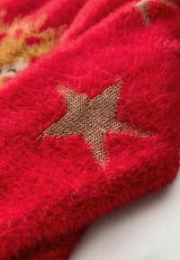 Red fuzzy textile featuring a prominent brown star pattern. The texture is soft and plush, with contrasting woven accents visible in the design.
