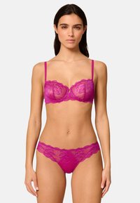 Ensemble de soutien-gorge en dentelle fuchsia et culottes assorties, avec des bords festonnés, des bretelles ajustables et des motifs floraux. La texture semi-transparente est prédominante.