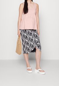 Ljusrosa linne med samlad midja, i сочетание med en svart och vit mönstrad kjol av medellängd med asymmetrisk fåll. Vita sandaler och en vävd väska.