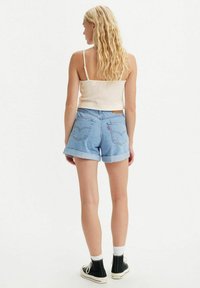 Pantalones cortos de mezclilla azul claro con dobladillos enrollados, que cuentan con bolsillos traseros y una etiqueta de cuero, combinados con una camiseta sin mangas de canalé beige.