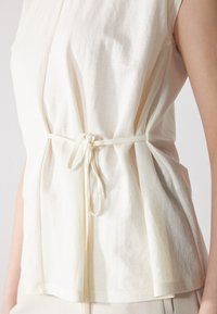 Bluzka w kolorze kremowym z krótkim rękawem i związanym w talii paskiem. Miękki, lekki materiał, o luźnym kroju i subtelnej fakturze.