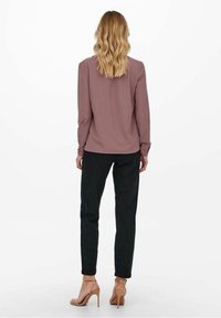 Maglia a maniche lunghe di color malva con un taglio rilassato, abbinata a pantaloni neri. Dettagli notevoli includono un taglio dritto e accenti di cuciture sottili.