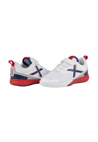 Zapatillas blancas con acentos en rojo y azul marino, laterales de malla, suela gruesa blanca y lengüeta trasera roja. Presenta un logo y detalles de costura en contraste.