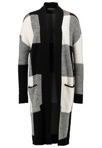 Cardigan oversize in bianco e nero con un motivo geometrico, dotato di tasche e polsini a coste. Texture in maglia morbida, design aperto davanti.