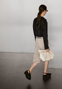 Svart jacka, beige mockaläder culotter, svarta plattformssandaler och en gräddfärgad handväska. Snygg design, strukturerad form och kontrasterande texturer.