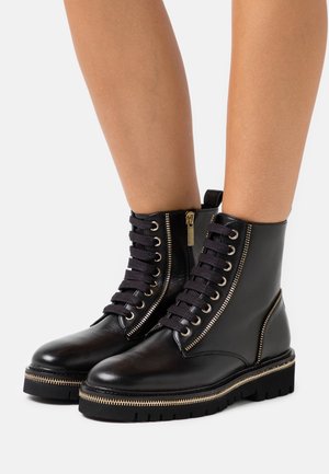 Stivaletti neri in pelle con zip laterale, lacci davanti, dettagli in metallo dorato e una spessa suola in gomma nera.