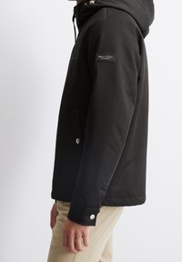 Czarna ocieplana kurtka z kapturem, zapinana na zamek, z bocznymi kieszeniami i naszywką z logo na rękawie. Gładka, matowa faktura.