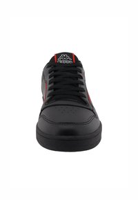 Chaussure de sport noire avec une tige en cuir lisse, des accents rouges, un bout rond et une semelle en caoutchouc plate. Elle dispose de lacets noirs et de perforations sur le bout.