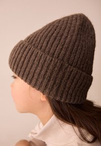 Brown ribbed wool beanie with a slouchy design, featuring a thick cuff and soft texture, carefully fitted on a side-profile view.