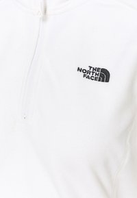 Biały polarowy pulower z zamkiem błyskawicznym z przodu, z czarnym haftowanym logo na lewej piersi i teksturowanym materiałem dla zapewnienia ciepła.