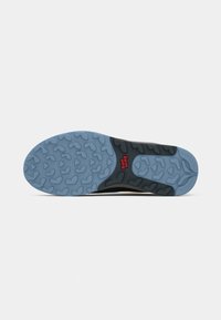 A sola de um sapato apresenta um fundo de borracha azul texturizada com padrões em forma de coração e uma entressola preta. Logotipo vermelho "Vans" visível.