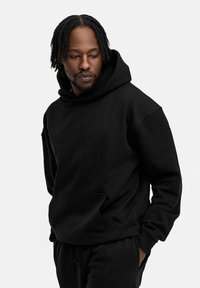 Schwarzer Hoodie aus weichem Gewebe, mit einer großen Fronttasche, Kordelzugkapuze und gerippten Bündchen. Glatte Textur, lässige Passform.