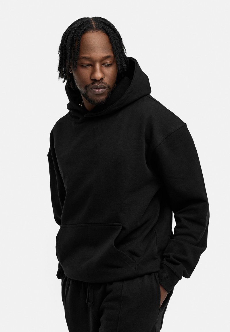 Schwarzer Hoodie aus weichem Gewebe, mit einer großen Fronttasche, Kordelzugkapuze und gerippten Bündchen. Glatte Textur, lässige Passform.