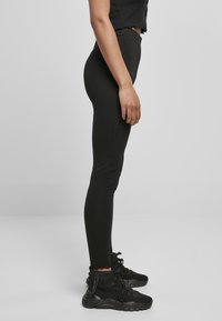 Zwarte leggings gemaakt van rekbaar materiaal, ontworpen met een hoge taille. Gepaarde met zwarte sportschoenen met een chunky zool en veters.