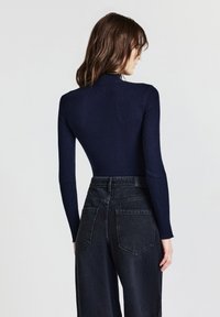 Maglia a maniche lunghe a costine color navy con colletto alto, abbinata a jeans neri a vita alta con gamba larga, dotati di tasche posteriori e finitura testurizzata.