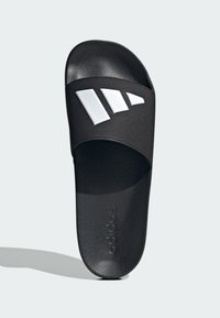 Crna klizna sandala s teksturiranom trakom koja sadrži tri bijele dijagonalne pruge. Podstava je također crna, s embossed natpisom "adidas" na đonu.