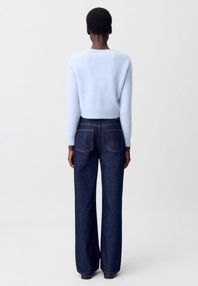 Pullover corto azzurro realizzato in morbido materiale, abbinato a jeans a gamba larga in denim scuro con vita alta, caratterizzati da tasche posteriori visibili e cuciture.