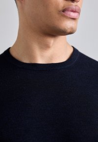 Mörkblå stickad tröja med rund hals och en slät textur, med en passande krage och subtila färgvariationer.