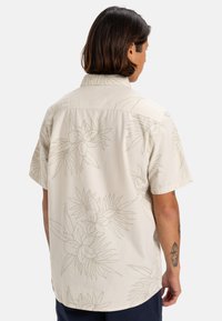 Camicetta beige a maniche corte con disegni floreali a linee, dotata di colletto a punta e vestibilità comoda, realizzata in cotone leggero.